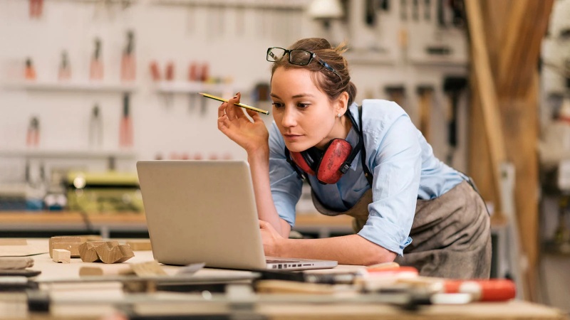 Woman working on laptop in workshop with protective headphones
