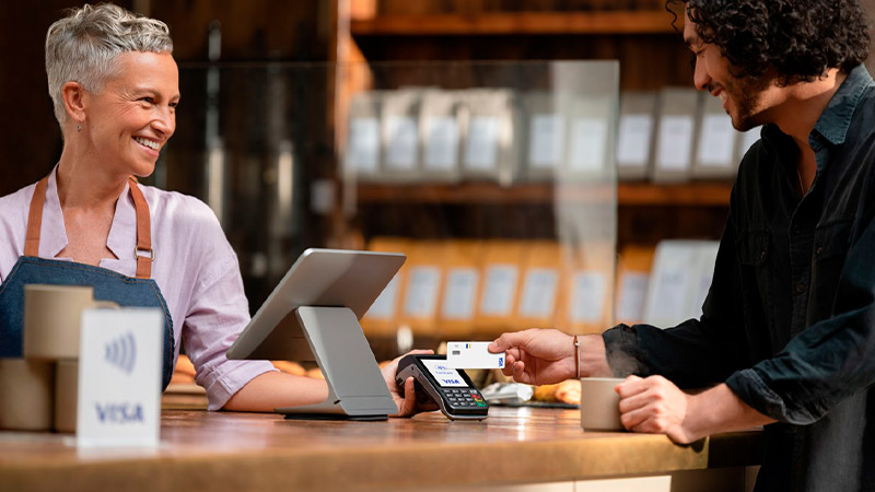 mujer atendiendo un negocio sonriendole al hombre que esta pagando con su tarjete visa 